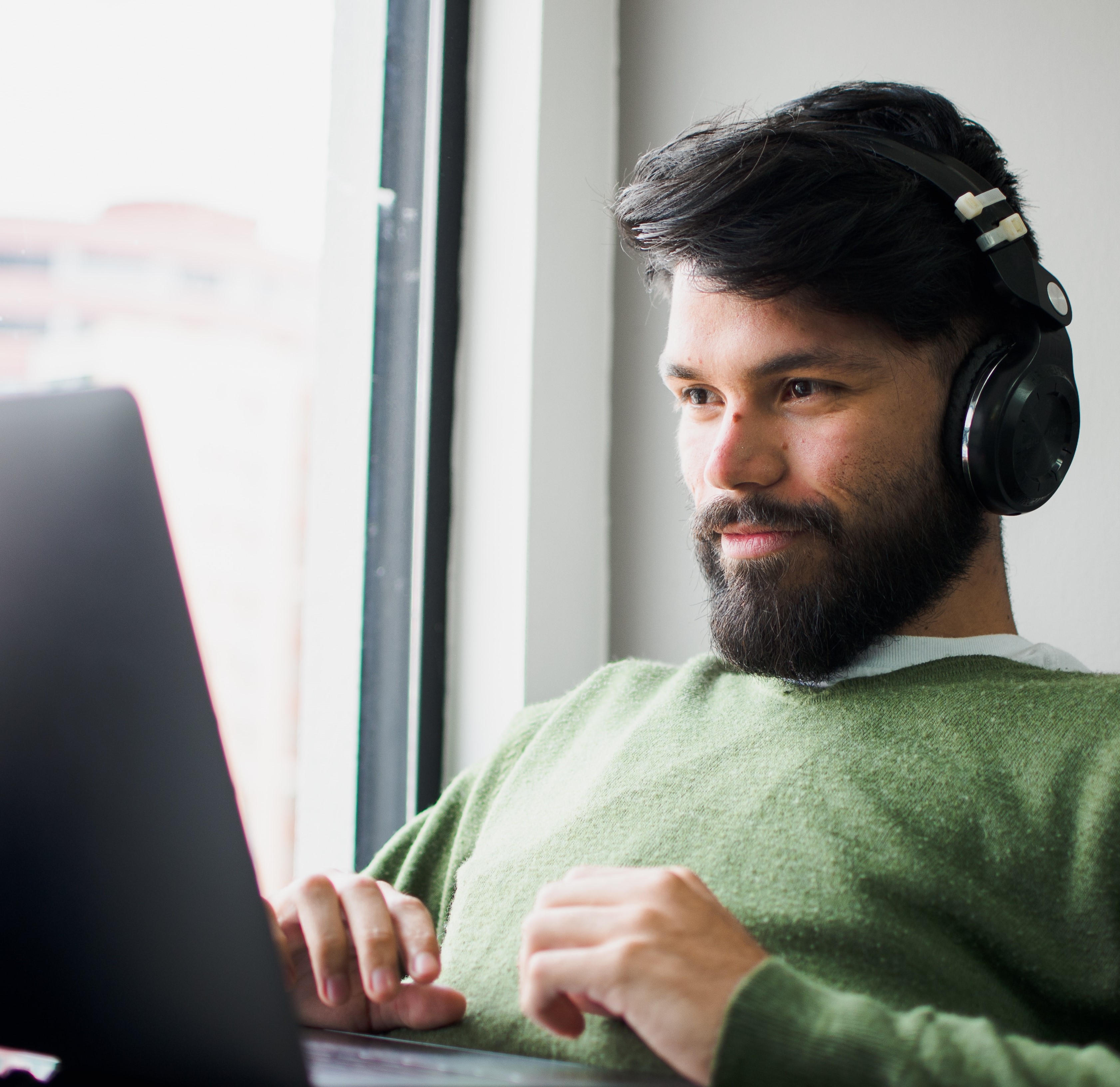 Youngish person sitting at laptop wearing headphones and smiling