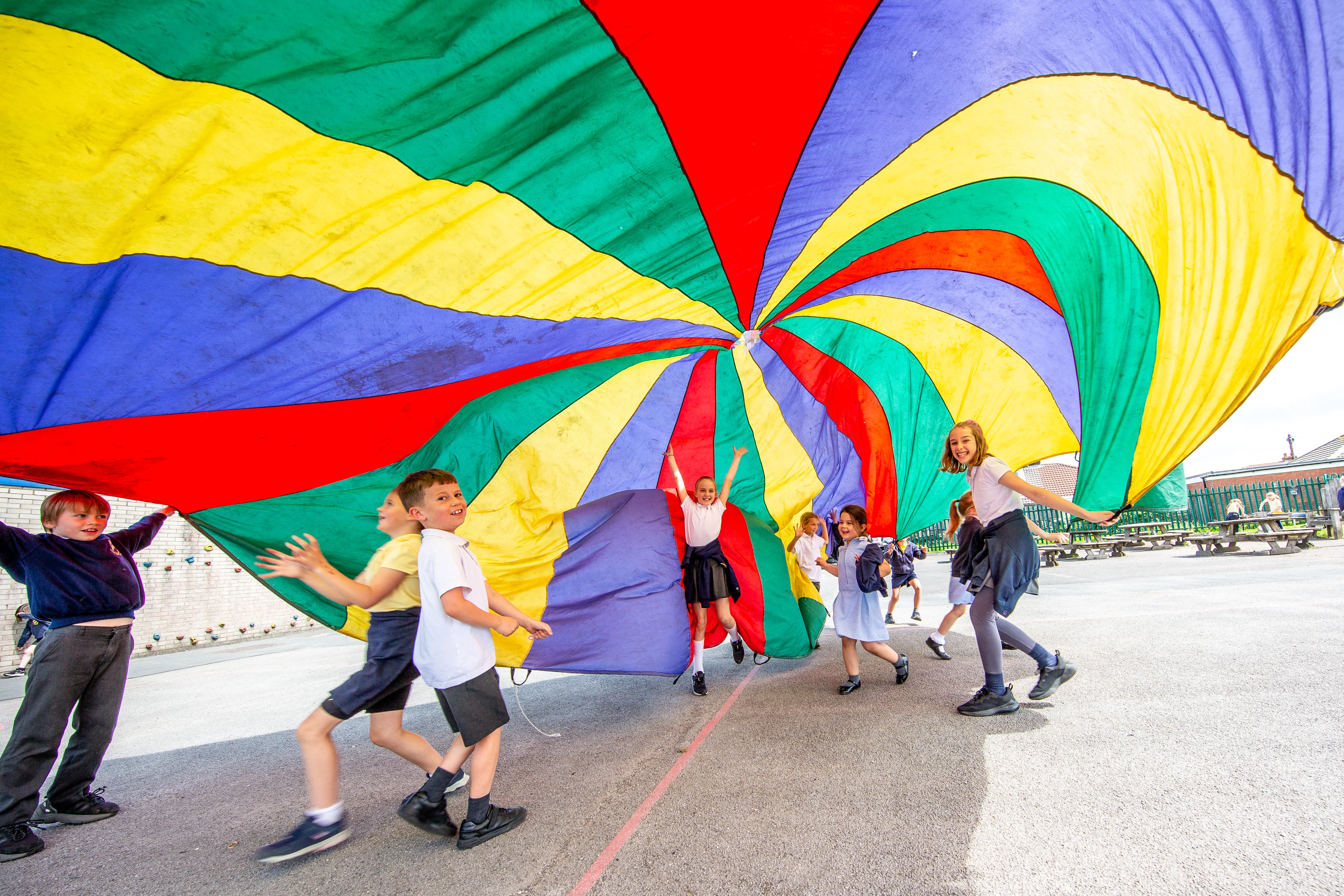 Children in school running under a colourful parachute
