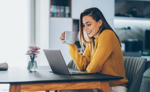 Woman smiling at a laptop holding a tea